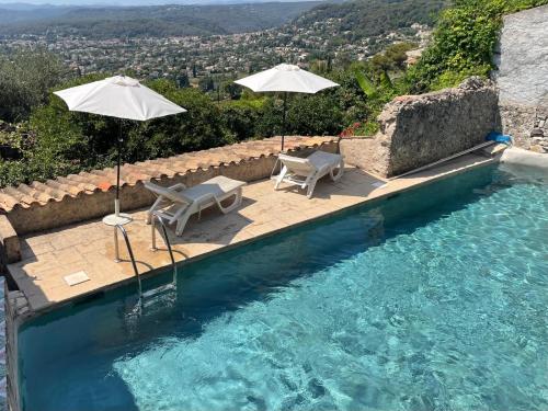 - une piscine avec 2 chaises longues et 2 parasols dans l'établissement La Petite Maison, à Saint-Paul-de-Vence