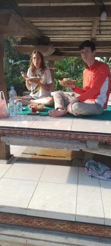 タバナンにあるTrinadhi Homestayのベンチに座って食事を食べる二人