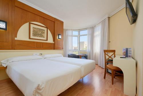 a bedroom with a large white bed and a desk at Hotel Pasarela in Seville