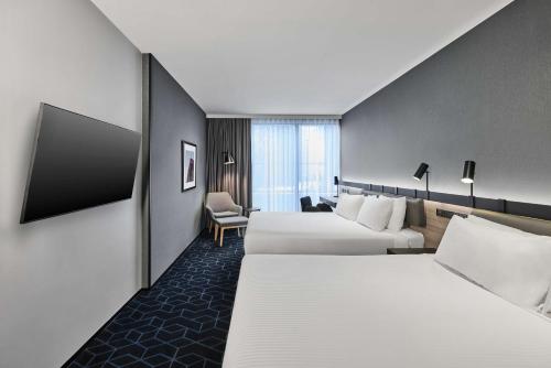 a hotel room with two beds and a chair at Vibe Hotel Melbourne Docklands in Melbourne