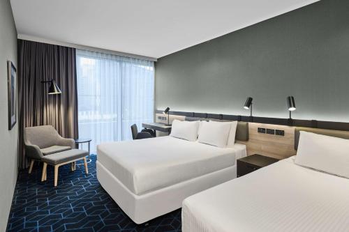 a hotel room with two beds and a chair at Vibe Hotel Melbourne Docklands in Melbourne