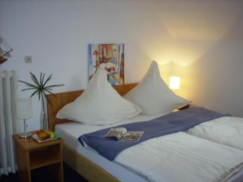 Una cama con almohadas blancas y un libro. en Hotel Garni Zentral en Willich