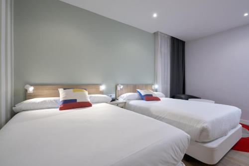 two beds in a hotel room with white sheets at Hotel Pasarela in Seville