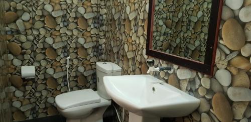 baño con lavabo, aseo y pared de piedra en AHSRAM Accommodations, en Pasikuda