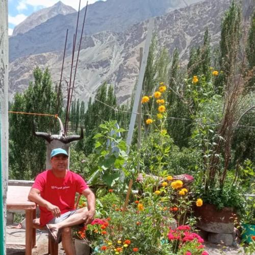 a man sitting in front of a garden with flowers at Summer and winter homestay Turtuk Youl in Turtok