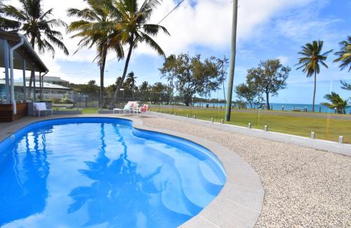 a swimming pool with palm trees and the ocean at Iluka Palms in Grasstree Beach