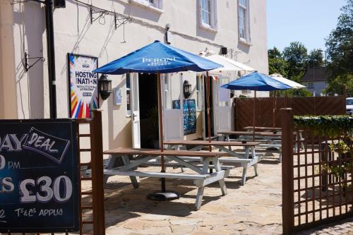 a row of wooden tables with umbrellas in front of a building at Sun Hotel by Greene King Inns in Hitchin