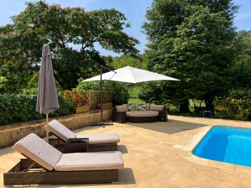 an umbrella and chairs next to a swimming pool at La Tuilerie Grange (Adults only gite) with two en-suite double bedrooms in Le Bugue