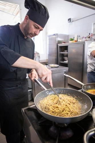 a man in a kitchen preparing pasta in a wok at Hotel Parrini in Follonica