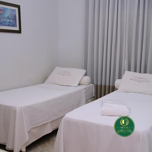 two beds with white sheets in a room at Hotel Gaucha in Guaíra