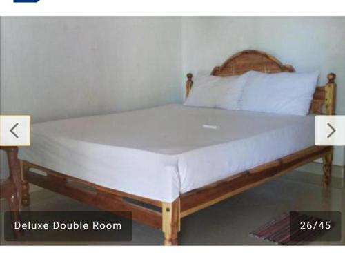 a large bed with a wooden frame and white sheets at Pranu House in Nilaveli