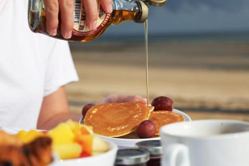 a person pouring syrup onto a plate of pancakes and fruit at Le Clos Normand in Saint-Aubin-sur-Mer
