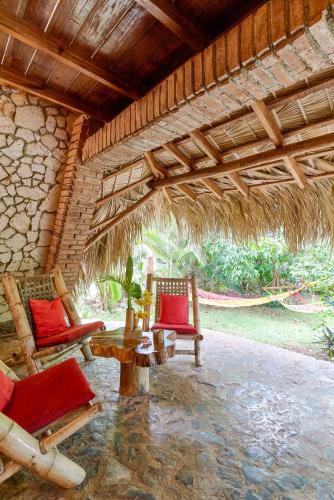a patio with two chairs and a table and a straw roof at CHALET TROPICAL Hotel & Restaurant-Pizzeria in Las Galeras