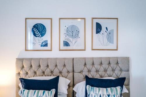 four framed prints on a white wall above a bed with four pillows at NEW! Spacious 3-Bed Home in Newcastle-under-Lyme by 53 Degrees Property, Ideal for Business, FREE Parking! in Newcastle under Lyme
