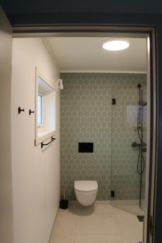 a bathroom with a toilet and a green tile wall at Gammelbutikken Guesthouse in Pettvik