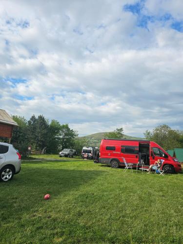 a red van parked in a grass field with cars at Konaci Očeva Zemlja Vikendica i Bungalovi in Mojkovac