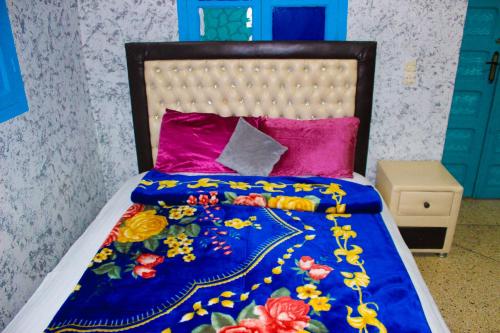 a bed with a blue comforter and pink pillows at Riad Dar Karaz in Sefrou
