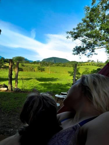 two women laying in a hammock looking out at a field at Chalé em Treviso Sítio Pé do Morro in Treviso