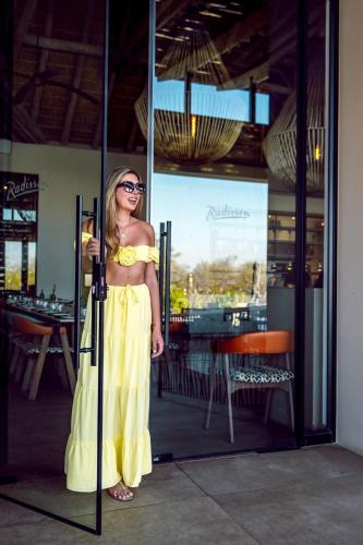 a woman in a yellow dress standing in front of a glass door at Radisson Safari Hotel Hoedspruit in Hoedspruit