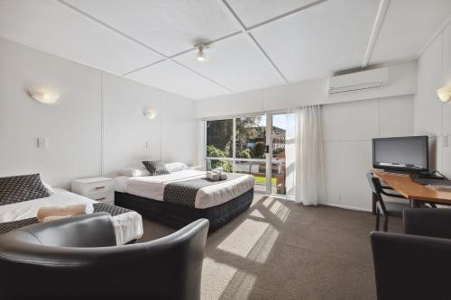 a bedroom with two beds and a desk and a tv at Flamingo Motel in New Plymouth