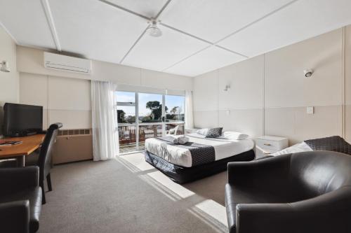a bedroom with two beds and a desk and a television at Flamingo Motel in New Plymouth