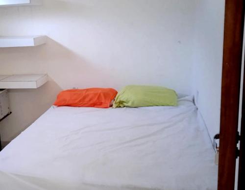 a white bed with an orange and green pillow on it at Hostel Summer Praia do Sol in João Pessoa