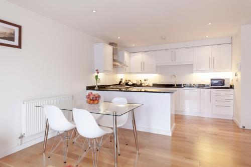 cocina con armarios blancos, mesa y sillas en Roomspace Serviced Apartments - Marquis Court en Epsom