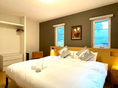 a bedroom with a large white bed with two windows at Wabi Sabi Chalet Hakuba in Hakuba