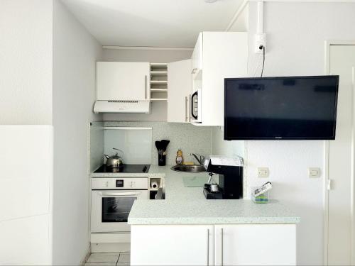 Il comprend une cuisine avec des placards blancs et une télévision murale. dans l'établissement Canet-en-Roussillon T2 Moderne - Climatisation - Parking privé - Plage à 2 pas! - FR-1-794-155, à Canet
