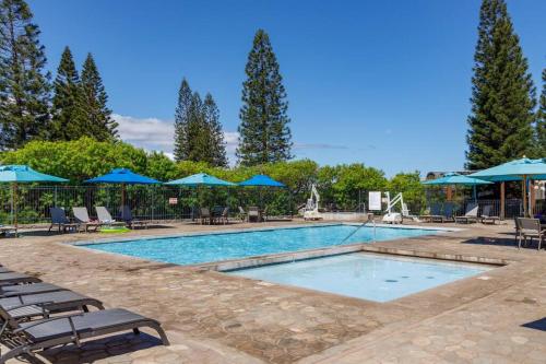 a swimming pool with chairs and blue umbrellas at 6 Bed 4 Bath Condo in Waikoloa Village in Waikoloa Village