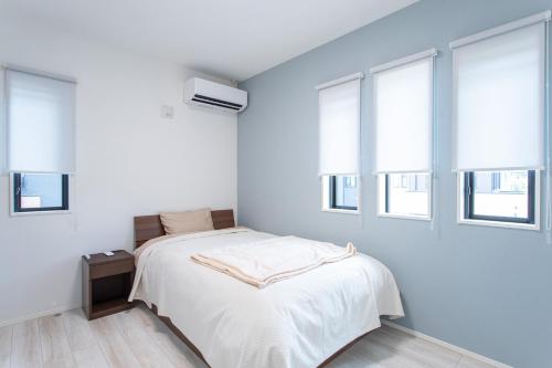 a white bedroom with a bed and windows at Mova Villa Okino in Kikuyo