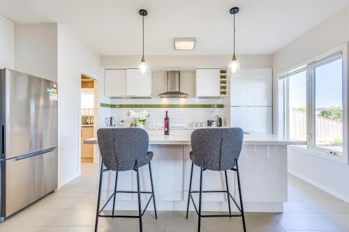 a kitchen with white cabinets and bar stools at StayAU Magnificent Lakefront Villa Stunning Views in Point Cook
