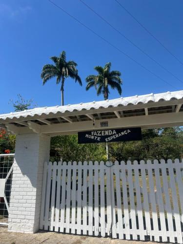 a white fence in front of a building with palm trees at Fazenda Monte Esperança in Guapimirim