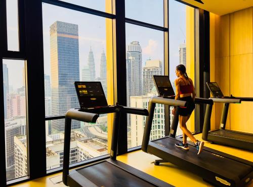 a woman on a treadmill in a gym looking out the window at Axon Residence KLCC - KL HOME in Kuala Lumpur