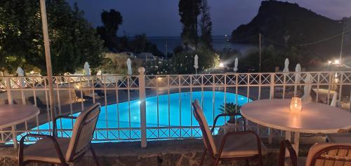 a pool with tables and chairs next to a fence at Paleo Inn Hotel in Paleokastritsa