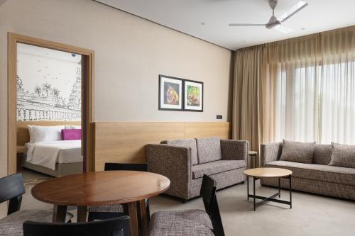 a hotel room with a table and a couch and a bed at Lilac Kumbakonam in Kumbakonam