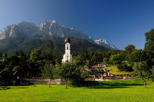 a church in a field with mountains in the background at Romantik Alpenhotel Waxenstein in Grainau