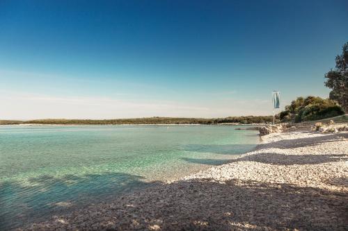 a beach with blue water and trees in the background at Camping Homes Mon Perin in Bale