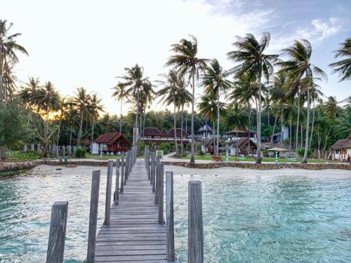 a wooden bridge over the water with palm trees at Arys Lagoon Bungalow & Hotel in Karimunjawa