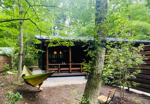 a person in a hammock in front of a cabin at 森の宿り 時庵 まるやま in Nasu