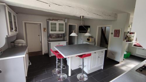 une cuisine avec des placards blancs et des tabourets de bar rouges dans l'établissement Logis de Vaux - Maison de campagne familiale spacieuse, à Madré
