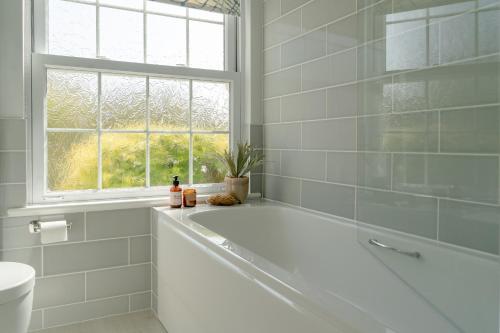 a white bathroom with a tub and a window at Sandpipers, Port Isaac Bay Holidays in Port Isaac