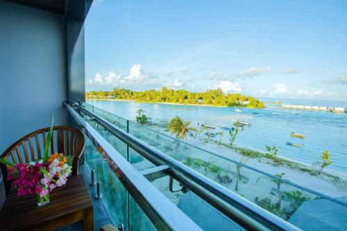 a balcony with a view of the ocean with a table and flowers at Beach Hotel Guraidhoo in Guraidhoo