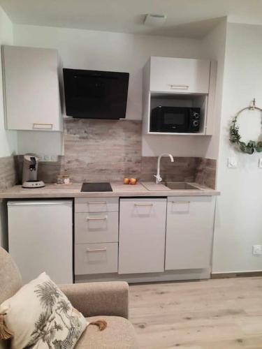 une cuisine avec des armoires blanches, un évier et un micro-ondes dans l'établissement Studio 3 - Appart' Hôtel tout confort avec balcon - TU ELLETA, à Tulette
