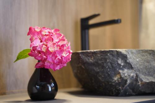 a black vase with a pink flower next to a rock at Suita beli Labod in Medvode