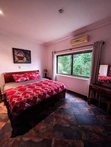 a bedroom with a bed with a red comforter and a window at Luxor garden Apartment 1A in Accra