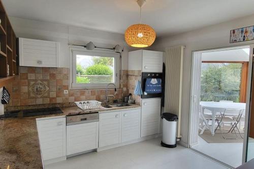 une cuisine avec des placards blancs, une fenêtre et une table dans l'établissement Villa Roz Granit Perros-Guirec, à Saint-Quay-Perros