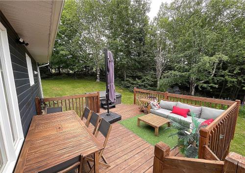 a wooden deck with a couch and tables and an umbrella at La Petite Ourse - boisé avec spa in Petite-Rivière-Saint-François