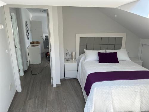 a white bedroom with a large bed with a purple pillow at Ático mirando o mar in Porto do Son