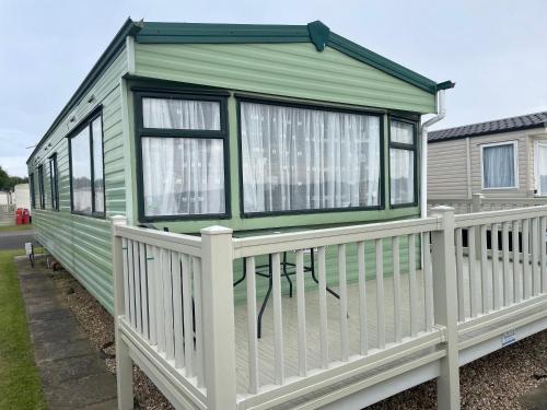 a green tiny house with a white fence at 4 Bed Lodge Sleeps 8 - Pet Friendly Parking in Skegness